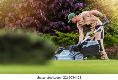 Caucasian Garden and Landscaping Worker Mowing  Backyard Lawn Using Electric Cordless Grass Mower. Garden Maintenance Theme. - Shutterstock ID 2268034421