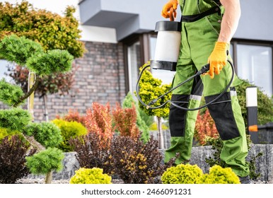 Caucasian gardener in protective suit spraying pesticide on tree and other plants inside a garden. - Powered by Shutterstock