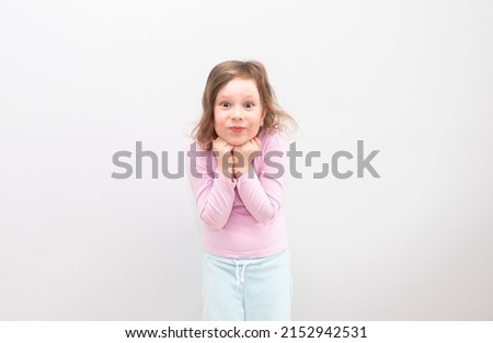 A Caucasian girl, 6 years old, in a pink T-shirt on a gray background. The child is happy and smiles and looks into the camera, emotions on his face.