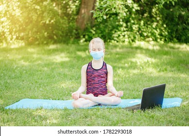 Caucasian Girl Child In Face Mask Doing Sport Workout Outdoor Online. Video Yoga On Internet. Kid Learning Training On Backyard At Home With Laptop. New Normal. Social Distance At Coronavirus.