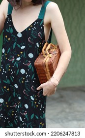 Caucasian Girl In Close Up Wearing Black Floral Dress With A Vintage Straw Bag Under Her Arm