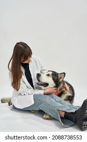 Caucasian Girl Embracing And Looking On Siberian Husky Dog In White Studio. Concept Of Relationship Between Human And Animal. Idea Of Owner And Pet Friendship. Adult Woman And Furry Dog. Copy Space