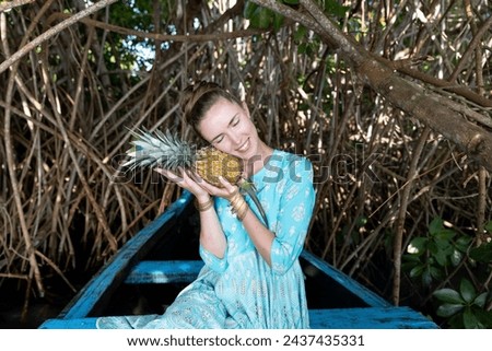 A Caucasian girl is enjoying her vacation in a warm country. She is holding a vitamin-rich pineapple. Going on vacation from winter to summer, enjoying the benefits of traveling to tropical countries
