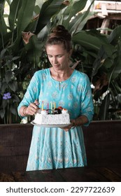 A Caucasian girl is holding a cake on her birthday. wearing a green dress.