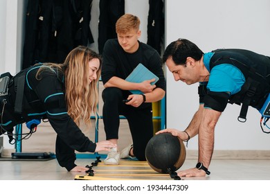 Caucasian girl and a middle-aged man exercising together while passing the medicine ball and also wearing an electrostimulation suit to lose weight - Powered by Shutterstock