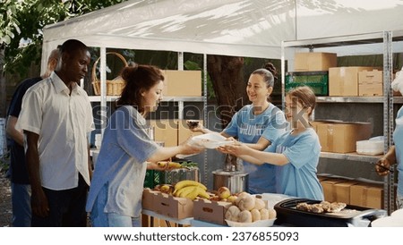 Caucasian girl packs free food to be distributed to the underprivileged with assistance from other charity workers. Female volunteers serving hot meals to the homeless and hungry at outdoor food bank.