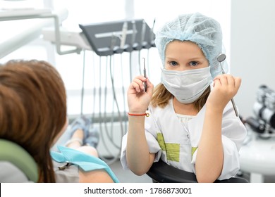 Caucasian Girl Playing At The Dentist. Child Holding Dental Instruments In Hands, Woman Dentist Depicts A Patient