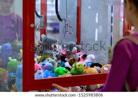 Caucasian girl playing toy crane vending machine, Claw Game or Cabinet to Catch the Toys. Shopping, holiday activity, game of chance, vacation concept. Selective focus on crane.
