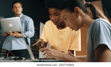 Caucasian girl programing or coding system while african boy fixing model. Teacher holding laptop while looking at diverse children writing web develop program. Innovation education. Edification. - Powered by Shutterstock