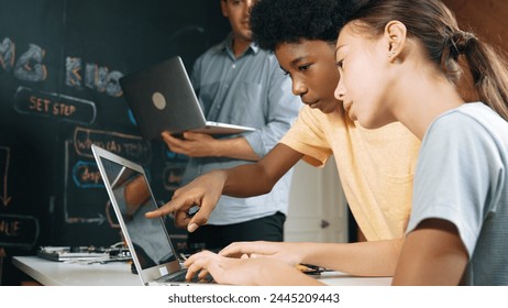 Caucasian girl programing or coding system while african boy fixing model. Teacher holding laptop while looking at diverse children writing web develop program. Innovation education. Edification. - Powered by Shutterstock