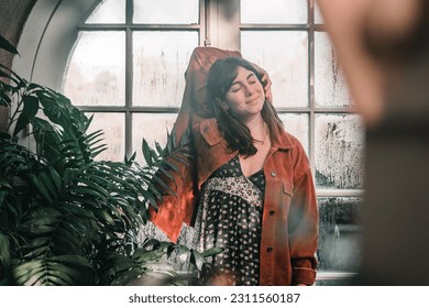 caucasian girl in red corduroy jacket standing smiling with eyes closed and right hand on her head calm and relaxed inside a botanic garden, botanic garden christchurch, new zealand - Shutterstock ID 2311560187