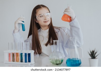 Caucasian Girl Student Learning A Chemical Experiment In Science Class. Cute Little Girl Holding Test Tube While Learning Chemistry Class In White Laboratory Room. Education And Science Concept.