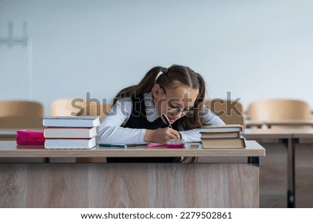 Caucasian girl with two ponytails sits at her desk and writes in a workbook.