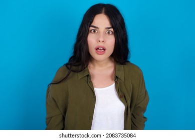 caucasian girl wearing trendy clothes standing over blue background  having stunned and shocked look, with mouth open and jaw dropped exclaiming: Wow, I can't believe this. Surprise and shock