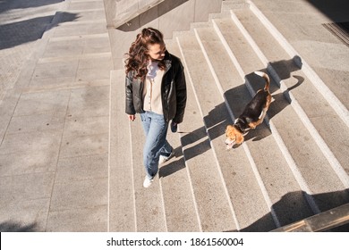 Caucasian Gorgeous Woman Looking At Her Dog While Walking With Him Down Stairs While Enjoying A Good Sunny Weather. Walking And Taking Care Of The Dog Concept