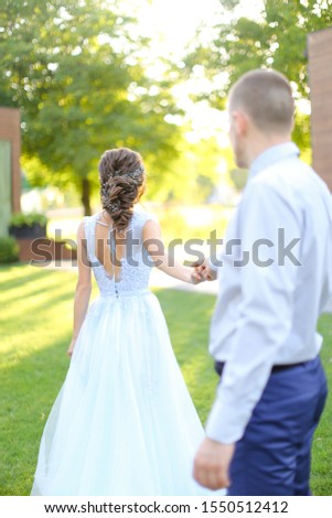 Caucasian groom following bride and walking in park holding hands. concept of wedding and bridal photo session in open air.
