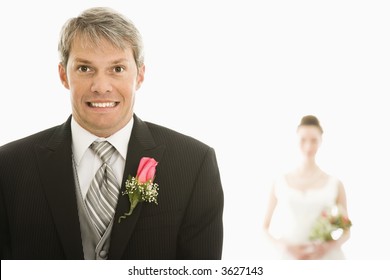 Caucasian Groom In Foreground With Scared Expression And Asian Bride In Background.