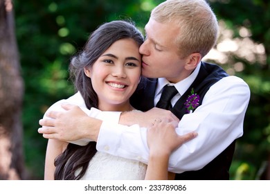 Caucasian groom lovingly kissing his biracial bride on cheek. Diverse couple - Powered by Shutterstock