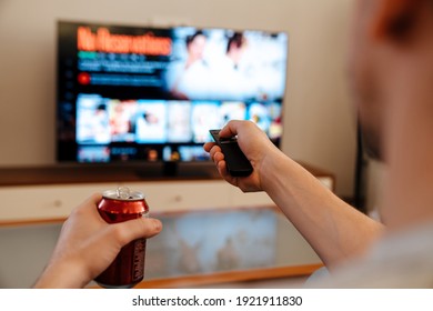 Caucasian Guy Drinking Soda And Using Remote Control While Watching TV At Home