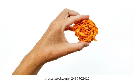 A Caucasian hand holds a ball of orange rubber bands, symbolizing office supply organization and creativity - Powered by Shutterstock