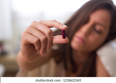 Caucasian hand of ill young brunette ill girl holding a pill of medicine for fever, headache, and chronic disease and with sadness face, with closed eyes - Shutterstock ID 1218622543