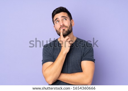 Caucasian handsome man having doubts while looking up over isolated purple background