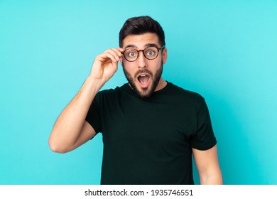 Caucasian handsome man isolated on blue background with glasses and surprised