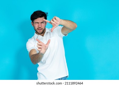 Caucasian Handsome Man Posing During Improvised Photoshot As Holding A Photocamera in Hands During Photosession and Looking Straight to camera Over Blue Background. Horizontal Image