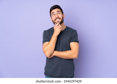 Ein gut aussehender, kaukasischer Mann, der eine Idee denkt, während er auf isoliertem violettem Hintergrund schaut