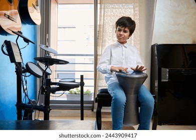 Caucasian handsome teenager, boy musician drummer banging drums tam tam bongo djembe, playing on traditional African ethnic percussion musical instrument in modern music studio interior - Powered by Shutterstock