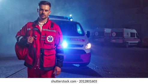Caucasian handsome young male paramedic in red uniform getting ready to work at night shift. Ambulance car on background. Good looking man doctor outdoors with backpack. Portrait. Call 911