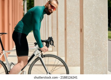 Caucasian Handsome Young Man In Protective Helmet Goes Out For Bicycle Ride Through City Streets On Blurred Background. Cyclist Male Ride Bike Outdoors In Urban.