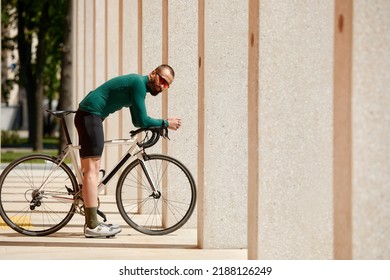 Caucasian Handsome Young Man In Protective Helmet Goes Out For Bicycle Ride Through City Streets On Blurred Background. Cyclist Male Ride Bike Outdoors In Urban.