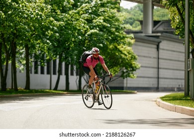 Caucasian Handsome Young Man In Protective Helmet Goes Out For Bicycle Ride Through City Streets On Blurred Background. Cyclist Male Ride Bike Outdoors In Urban.