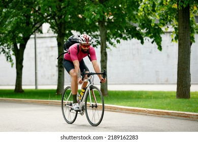 Caucasian Handsome Young Man In Protective Helmet Goes Out For Bicycle Ride Through City Streets On Blurred Background. Cyclist Male Ride Bike Outdoors In Urban.