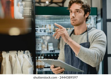 Caucasian handsome young shop assistant owner barista bartender waiter checking the quality of goods, doing inventory with notepad in small cafeteria coffee shop - Powered by Shutterstock