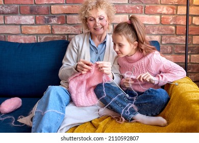 Caucasian happy family knitting. Senior woman and child girl, grandmother is teaching little girl to knit. Crafts for kids. Using Knitting tools, needles, have talk while sitting at home on sofa