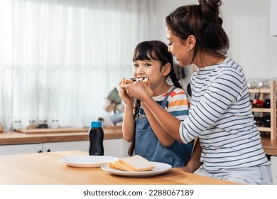 Caucasian happy family, parent spend time with kid together at home. Young girl daughter eatting sweet chocolate and bread with mother with happiness in kitchen. Activity relationship in house concept - Powered by Shutterstock