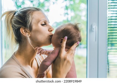 Caucasian Happy Loving Mother Holding Her First Child, Tiny Newborn Son, In The Air And Kissing Him While Standing Near The Window At Home. High Quality Photo