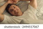 Caucasian happy man sleeping open eyes wake up looking at camera smiling good morning comfortable cozy guy rest relaxation bedroom bed hotel wellbeing positive weekend male pleasure home satisfaction