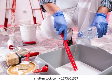 Caucasian House Painter Worker In White Overalls, Prepare The White Paint To Paint The Pink Wall. Construction Industry. Work Safety.