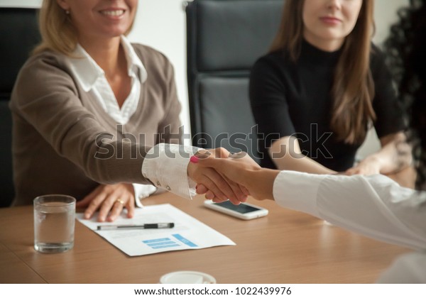 Caucasian hr manager welcoming african applicant\
at job interview, diverse businesswomen handshaking at group\
meeting, good first impression and female teamwork, women business\
partnership concept