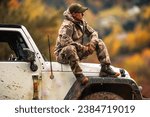 Caucasian Hunter in His 40s Seating on the Hood of His All Wheel Drive Vehicle During Hunting Day