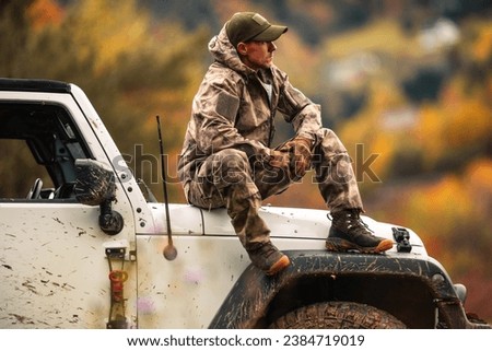 Caucasian Hunter in His 40s Seating on the Hood of His All Wheel Drive Vehicle During Hunting Day