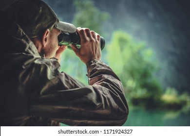 Caucasian Hunter in Masking Camouflage Uniform with Binoculars. Hunter Spotting Game. Poacher or Soldier Clothing.