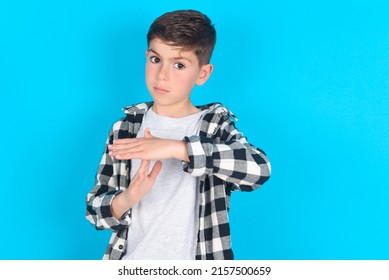 caucasian kid boy wearing plaid shirt over blue background feels tired and bored, making a timeout gesture, needs to stop because of work stress, time concept.