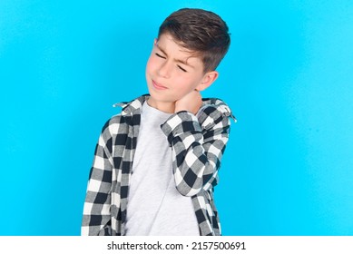 caucasian kid boy wearing plaid shirt over blue background suffering from back and neck ache injury, touching neck with hand, muscular pain. - Shutterstock ID 2157500691