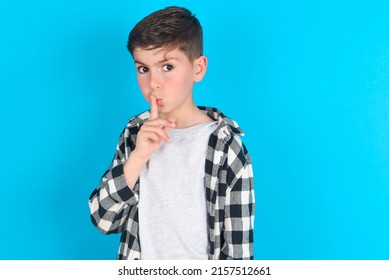 Caucasian Kid Boy Wearing Plaid Shirt Over Blue Background Makes Hush Gesture, Asks Be Quiet. Don't Tell My Secret Or Not Speak Too Loud, Please!