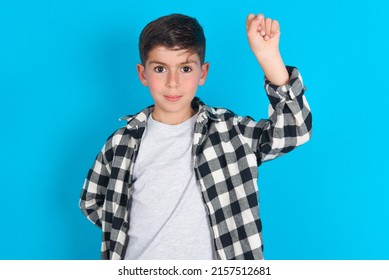 Caucasian Kid Boy Wearing Plaid Shirt Over Blue Background Feeling Serious, Strong And Rebellious, Raising Fist Up, Protesting Or Fighting For Revolution.