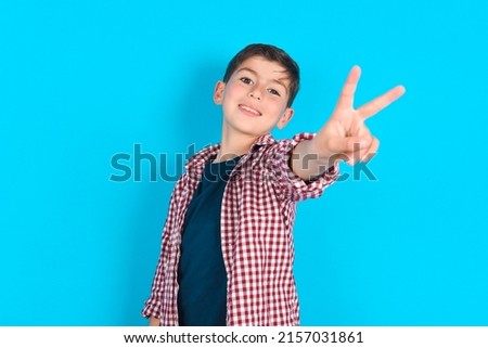 caucasian kid boy wearing plaid shirt over blue background directs fingers at camera selects someone. I recommend you. Best choice